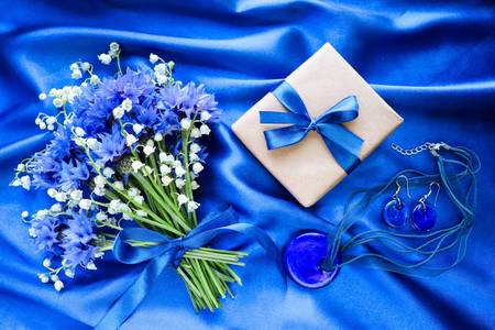 Flores y regalo sobre fondo de seda azul