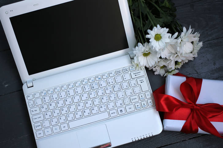 Белый ноутбук, цветы и подарок