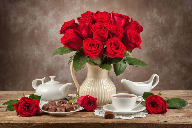 Blumenstrauß aus Rosen, Tee und Süßigkeiten auf dem Tisch
