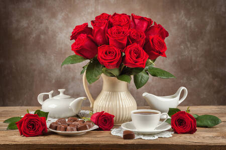 Bouquet of roses, tea and sweets on the table