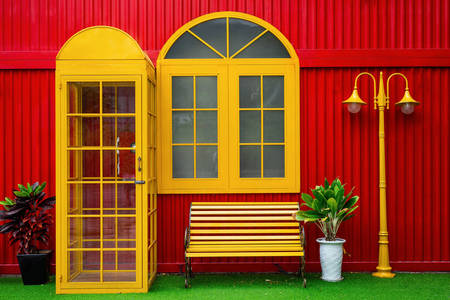 Yellow telephone booth and lamppost against red wall background