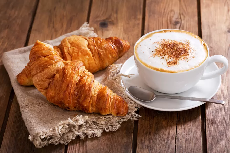 木のテーブルの上のクロワッサンとカプチーノ