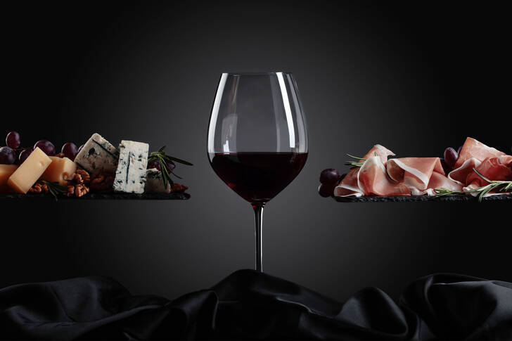 Glass of wine, cheese and prosciutto on a black background
